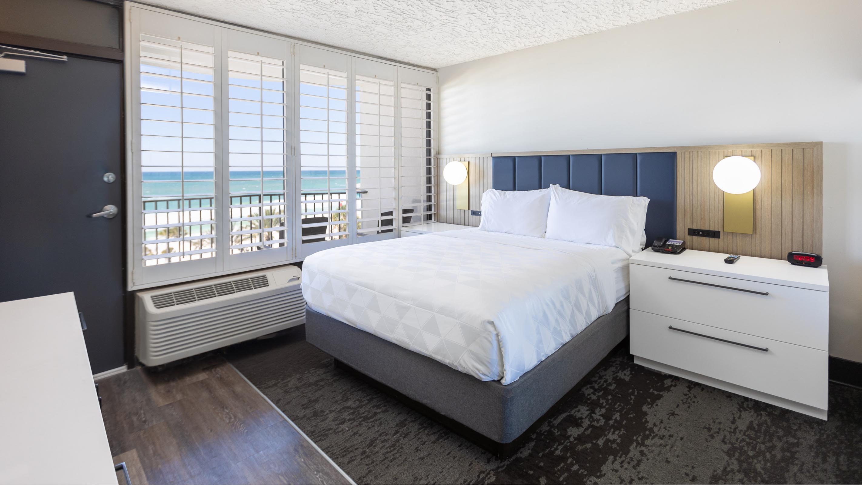 Queen bed with white side table and view of ocean