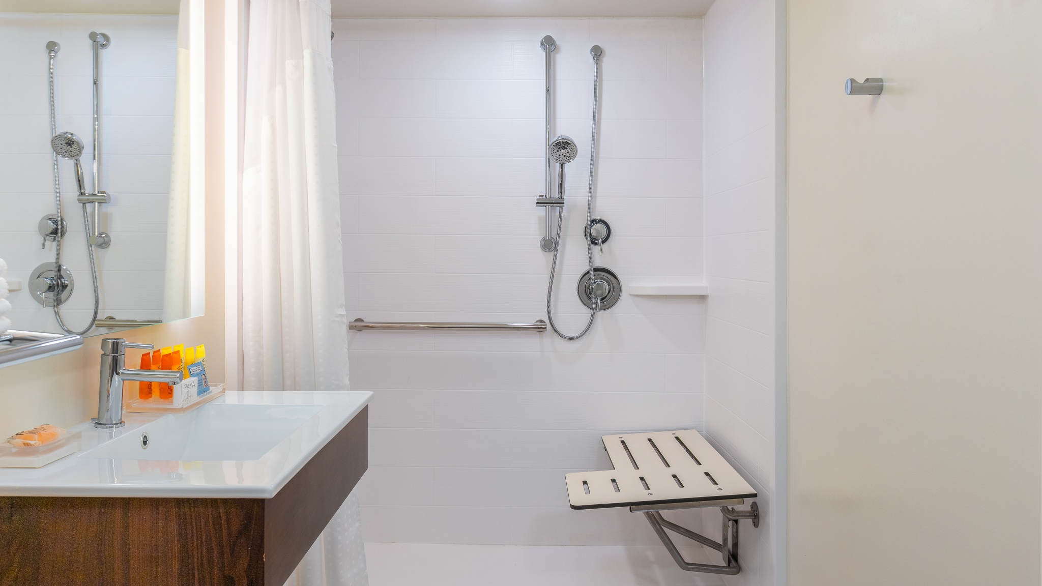 Accessible shower with grab bars, seat, handheld shower and lowered sink with lighted vanity